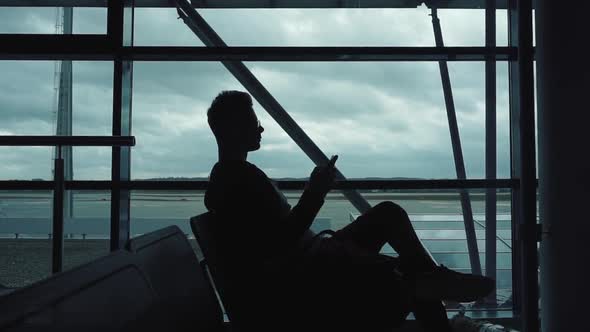 Silhouette of Man Listening To Music on Smartphone in Airport
