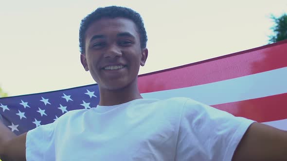 Afro-American teen boy with US flag smiling at camera outdoors alt
