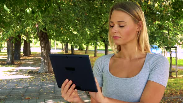 Young Pretty Blond Woman Works on Tablet - Park with Trees in Background alt