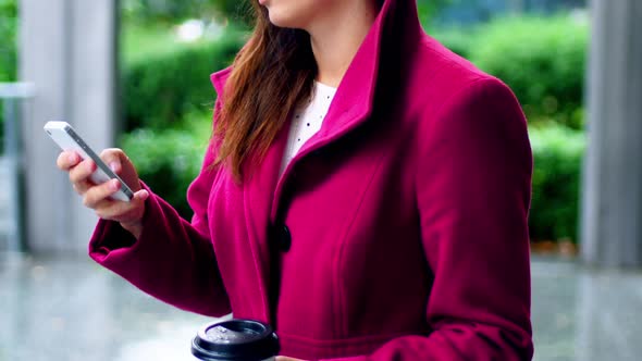 Businesswoman using mobile phone while having coffee alt