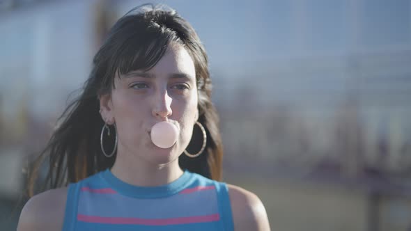 Close Frontal View of Darkhaired Girl Blowing Bubble with Chewing Gum alt