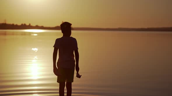 Boy with Red and green Paper Ships is walking in the river. Origami Paper Boats in kid's hands.  alt