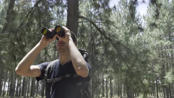 Hiker in forest looking through binoculars