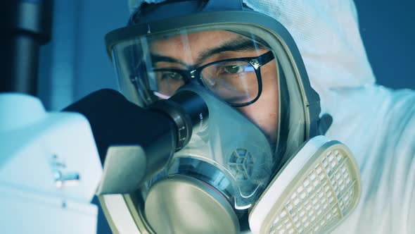 Male Specialist in a Hazmat Mask is Looking Into Microscope alt