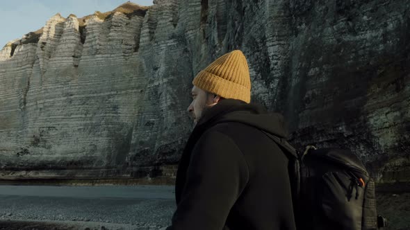 Camera Moves Around Happy Male Tourist Exploring Epic Sunny Rocky Beach, Looking for Inspiration alt