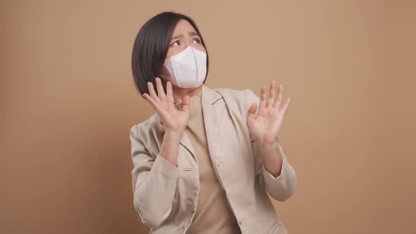 Asian business woman wearing hygienic mask scared and panic standing isolated over beige background.