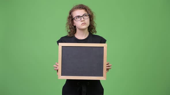 Young Happy Beautiful Nerd Woman Thinking While Holding Blackboard alt
