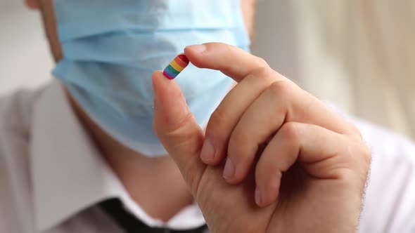 Man In Medical Mask And Suit Holding A Pill In The Colors Of The Rainbow Lgbt
