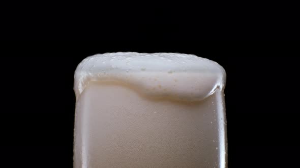 Pouring Lager Beer with Bubbles and Froth in Glass Over Black Background