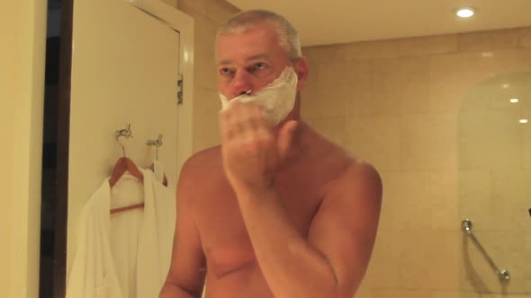 Man Applying Foam Shaving Gel to Face in Front of a Mirror