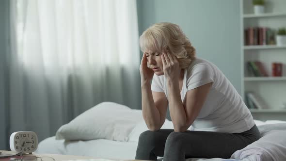 Senior Woman Sitting on Bed and Suffering From Terrible Headache, Health Problem alt