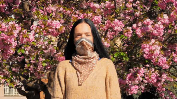 Adult Caucasian Woman in Mask on the Background Flowering Bushes alt