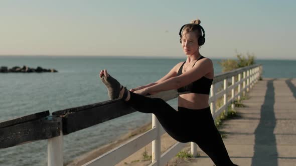 Woman in Sportswear Is Stretching Leg Putting It on Fence on River Waterfront. alt
