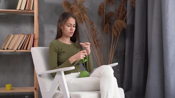 Focused Latin Woman Holding Needles Sitting on Armchair and Enjoying Knitting alt