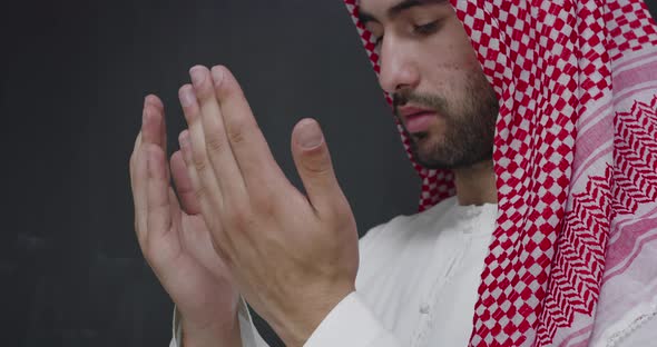 Man in Traditional Clothes in Front of Black Chalkboard Praying with Hands Wide Open alt