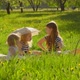 Three Blond Girls are Sitting on the Lawn in the Garden with Dog Running Around - VideoHive Item for Sale