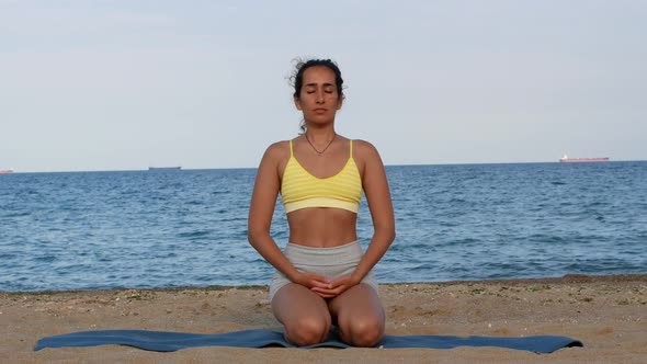 Beautiful tanned young woman sitting in a meditation pose on the beach. Goods for health. alt