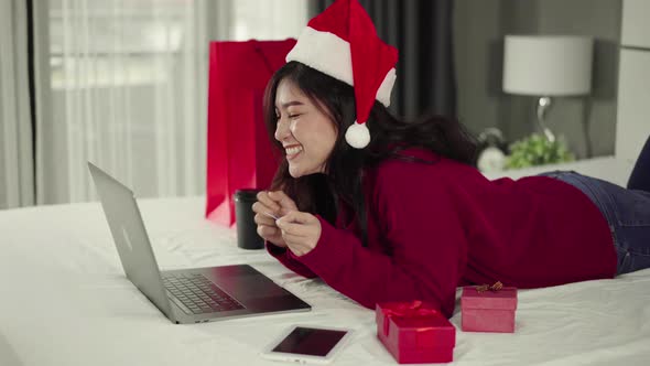 happy woman shopping online for Christmas gift with computer laptop and credit card on a bed