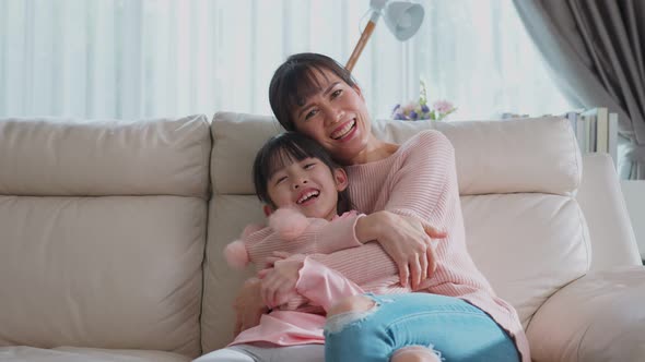 Portrait shot of lovely family Asian young little girl kid sit on sofa with mother in living room. alt