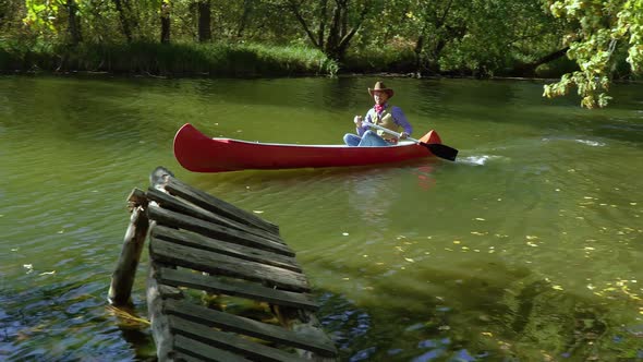 Cowboy in a Canoe Floats on the River in the Forest alt