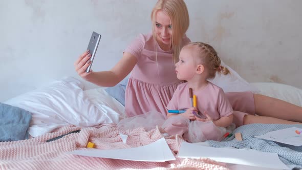 Young Attractive Blond Mom Take a Photo in Mobile Phone with Her Little Charming Daughter in Pink