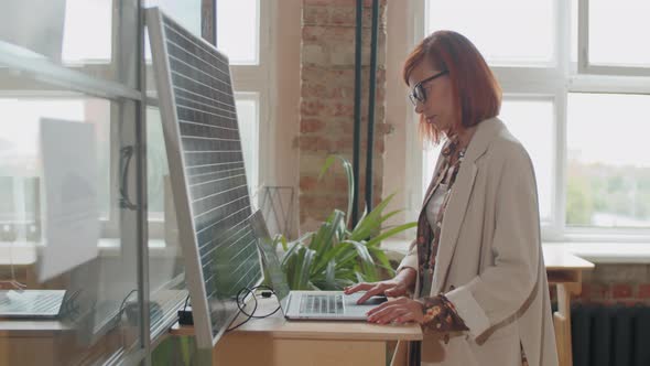 Businesswoman Charging Laptop with Solar Panel in Office alt