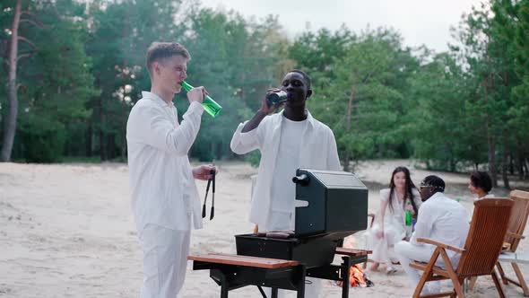 Handsome Young Men Cooking Barbecue at the Beach Party Drinking From Bottles