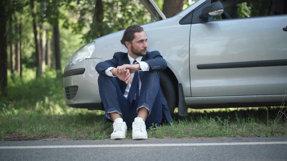 Front View Portrait of Stressed Male Driver Holding Head in Hands Sitting at Broken Car with Open alt