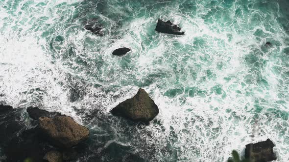 Aerial view 4k waves break on dark rocks near beach. Sea waves on the stones