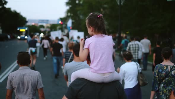 Daughter with father on political rally riot. Girls sits on parents shoulders.