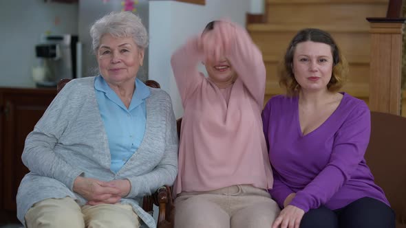 Portrait of Three Positive Caucasian Women of Different Ages Sitting on Couch at Home Looking at alt