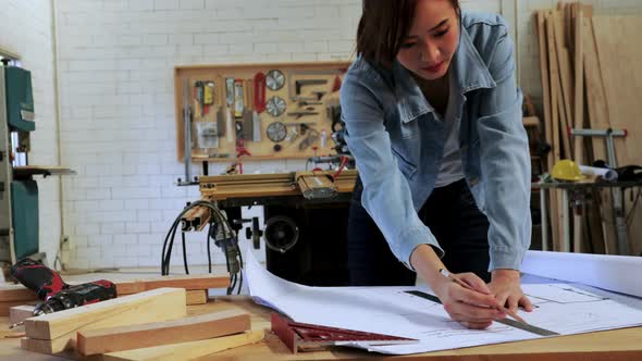 Carpenter female designing her wood construction project on drawing paper in workshop alt
