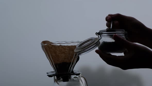 A woman putting ground coffee into a dripper to making drip coffee