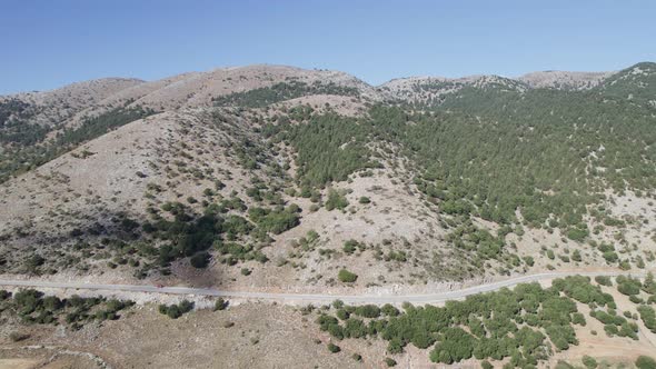 Aerial drone shot of the narrow curve road above rocky shore towards volcanic mountains. alt
