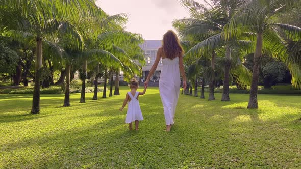 A Little Girl of Two Years Old in a White Dress Walks Her Mother Walk Hand in Hand Down a Park Trail alt