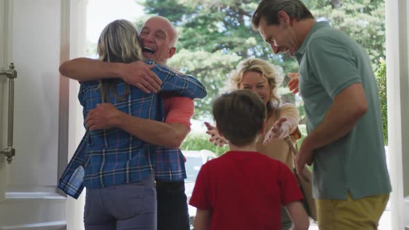 Happy caucasian couple with son opening door and greeting their grandparents alt
