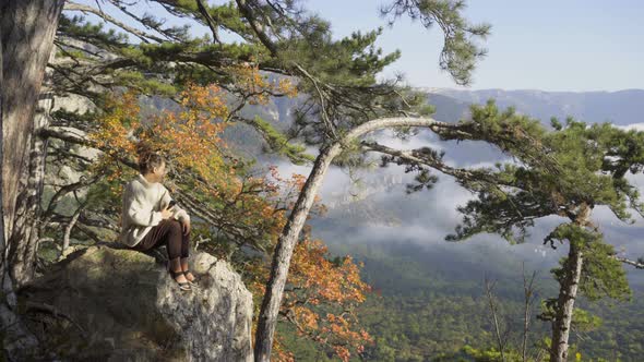 Woman in Loose Sweater Takes Picture of Landscape on Rock