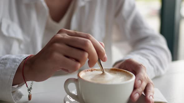 Hand Stirs Coffee Cappuccino With A Spoon Metal Spoon In A Cup Of Coffee Pushes The Foam And Whips alt