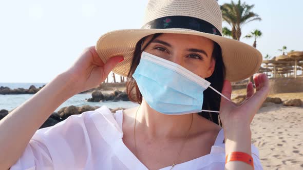 Portrait of Woman in Sun Hat, Who Takes Off Her Protective Mask, Against Sea Background, Beach  alt