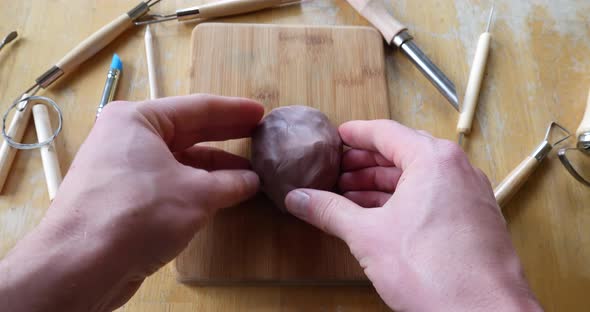A sculptor shaping and forming a face out of brown modeling clay in an art studio with tools on the alt