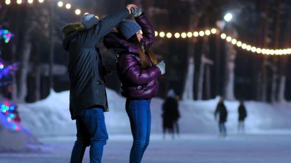 Happy Girl in Jacket Dances with Boyfriend on Skating Rink