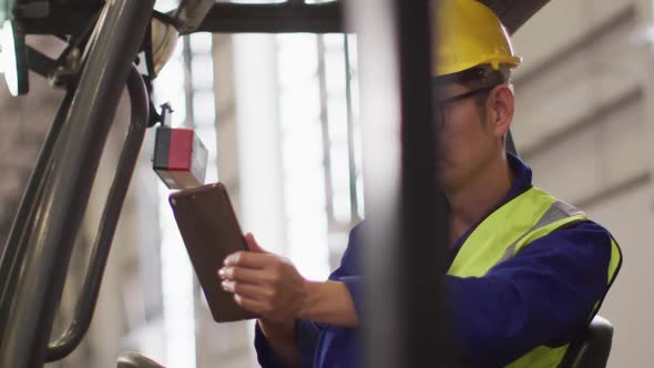 Asian male worker wearing safety suit with helmet using tablet in warehouse alt