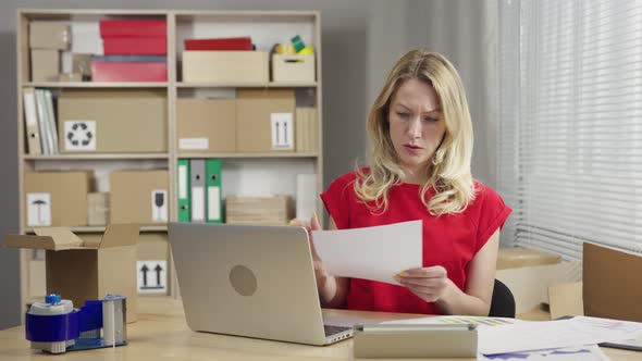 Warehouse Worker is Working in an Office Room Against Background of Boxes alt