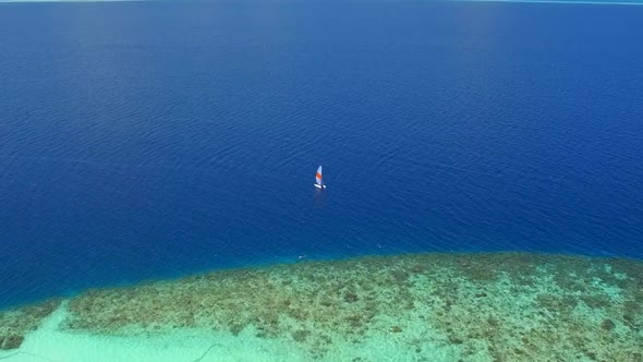 Aerial drone view of a man and woman sailing on a boat to a tropical island. alt