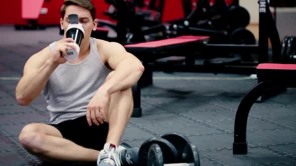 Young Man Athlete Drinking Water From Shaker Bottle in Gym alt