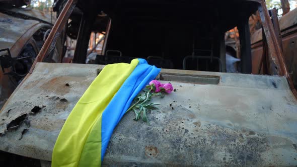 Ukrainian Flag and Purple Flowers on Car Hood of Burnt Out Destroyed Automobile alt