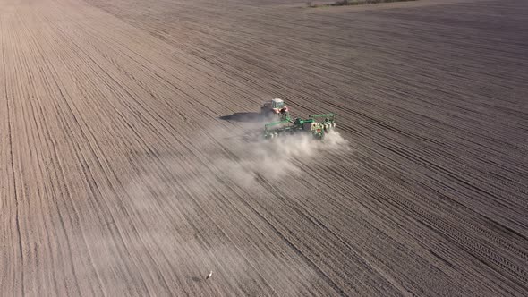 Aerial view of tractor with harrow system plowing ground on cultivated farm field alt