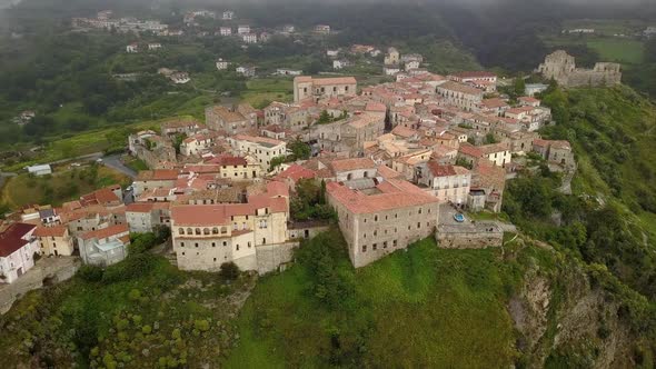 Aerial View Drone Flies Over Medieval Village on Hill Overlooking Misty Mountain Gorge. Cloudy Day alt