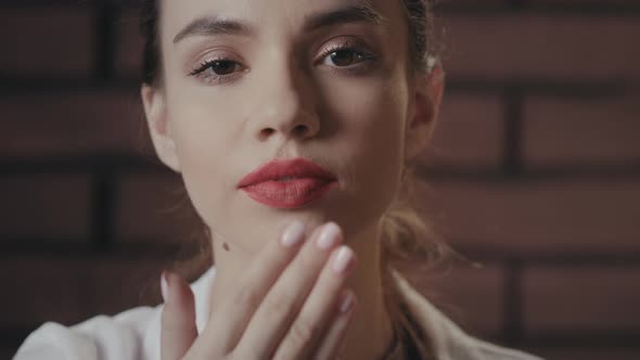 Sexy Woman with Red Lips Sending Kiss From Hand To Camera on Brick Background alt