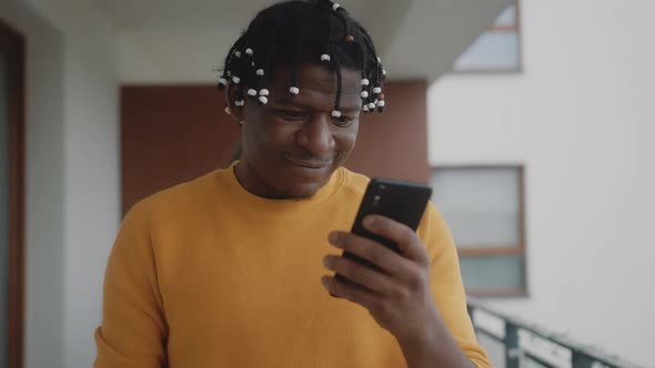 Portrait of Adrican American Black Man Checking Smartphone and Showing Gift Box alt